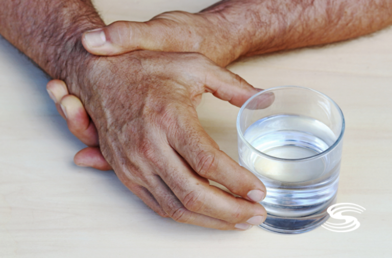 Older Man grabbing wrist to calm shaking in order to drink some water